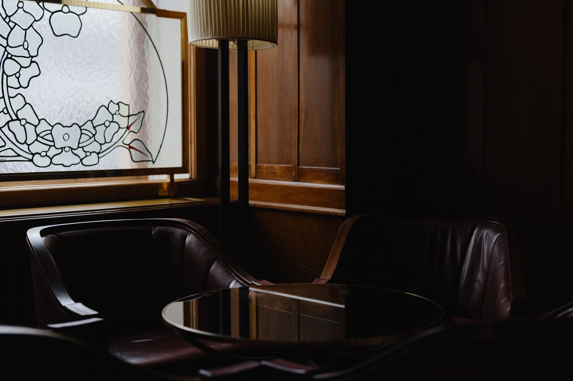 Sophisticated lounge interior with dark wood paneling and artistic stained glass window design.